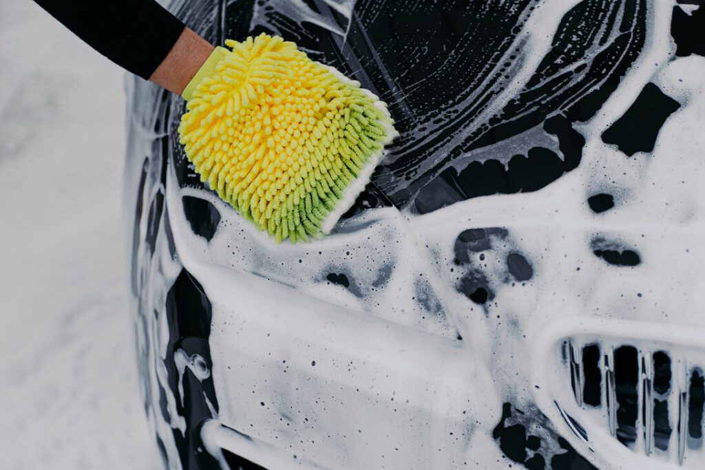 Unrecognizable man washes soapy black car with cloth at car station Man worker cleans automobile Vehicle and service concept