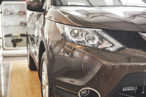 Close-up of a brown car's front end in a showroom, featuring the headlight and grille.