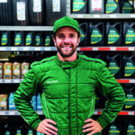 Man in a green racing suit stands with hands on hips in an auto parts store aisle.